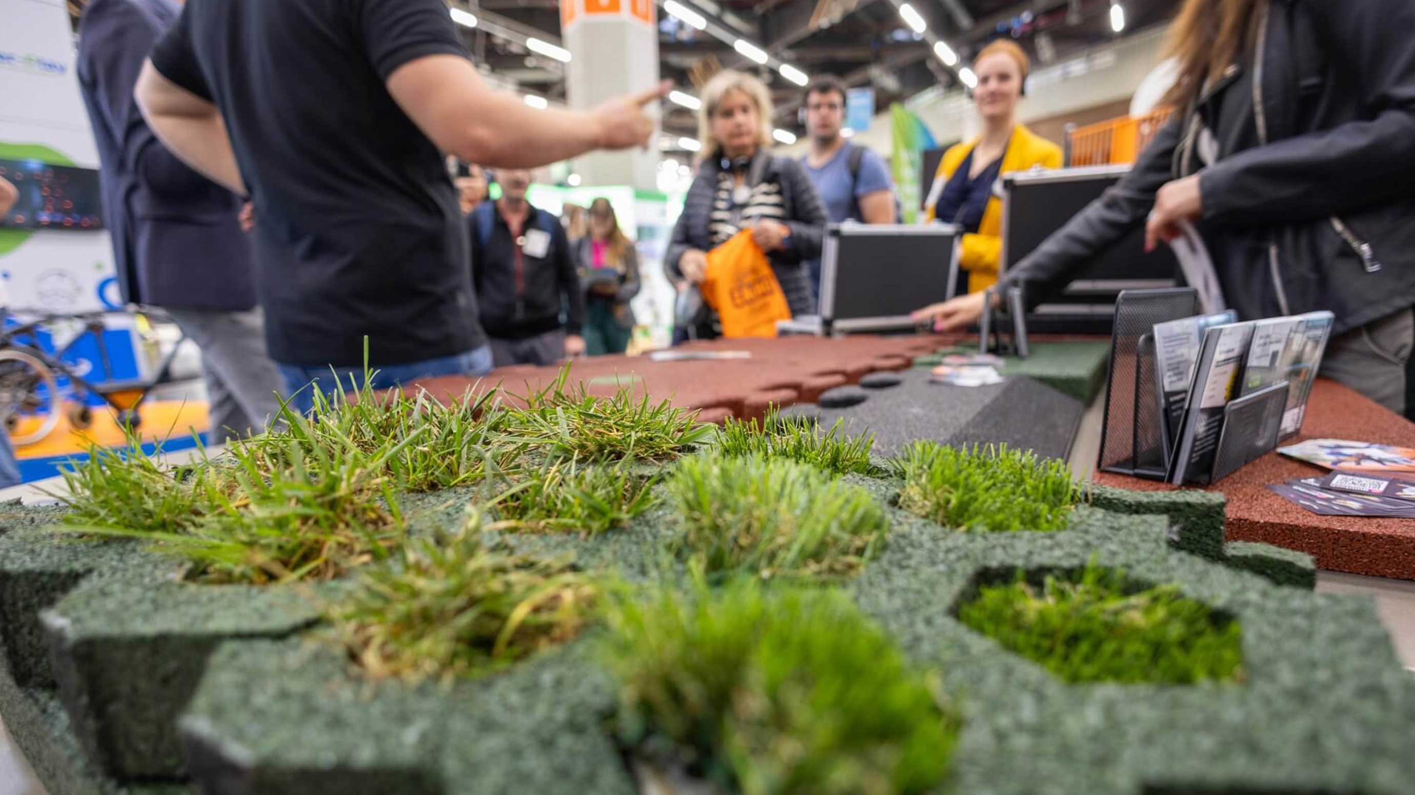 Messebesucher betrachten begrünte Flächen mit Gräsern und Gummiplatten