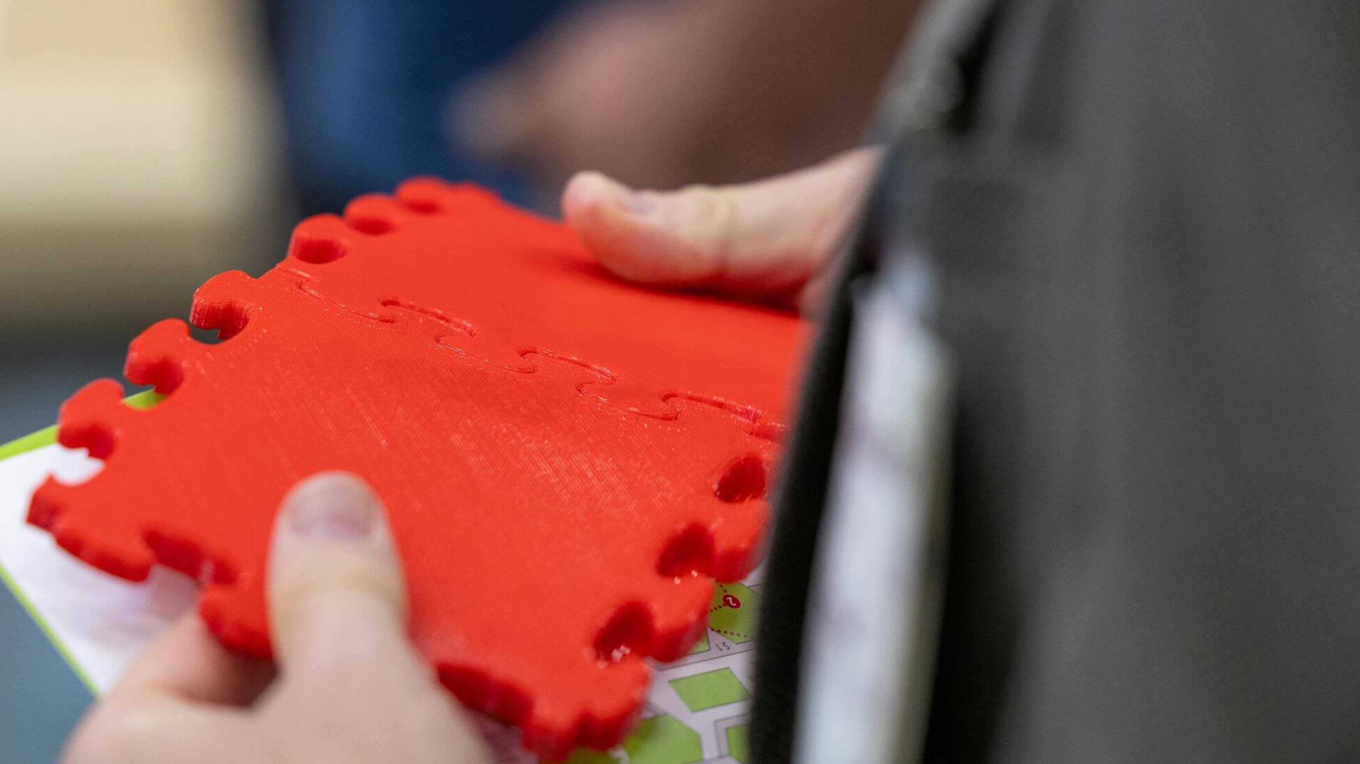 Zwei Hände halten ein rotes, modulares Kunststoffteil mit Stecksystem.